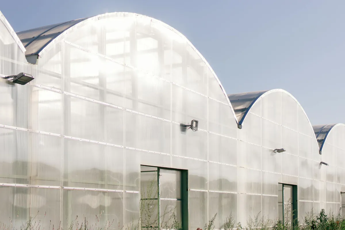 A freestanding arched-roof greenhouse standing on its own under a clear blue sky