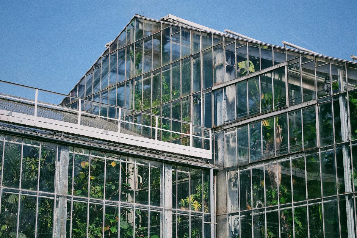 A freestanding glass greenhouse standing in the open under a clear blue sky