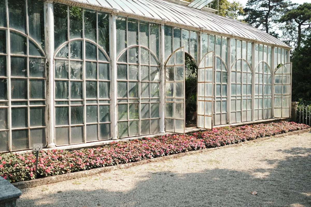 A glass greenhouse surrounded by blooming flowers in a sunny garden