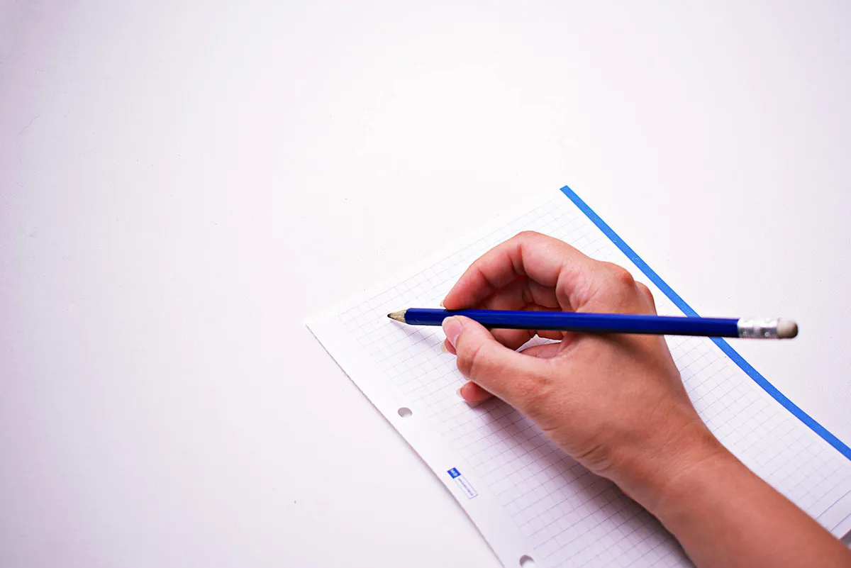 A hand sketching with a blue pencil on gridded graph paper