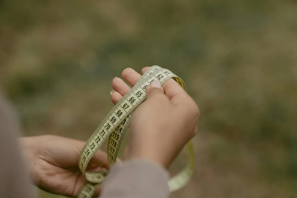 A pair of hands holding an extended yellow tape measure with the markings in focus